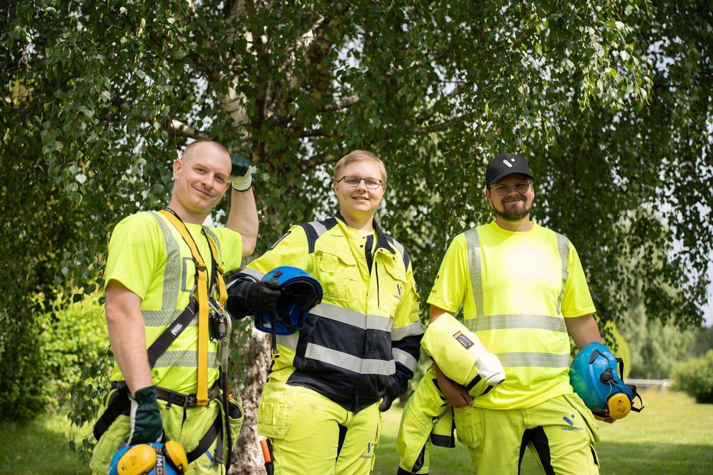 Kolme Vatajankosken sähköasentajaa. Taustalla koivu ja kesäinen maisema